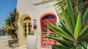 A building with two arched doors, one yellow and one red, and a large white planter in front. - Gozo Couples Bungalow No 3 · Pool Use & Own Cabana (Gozo)