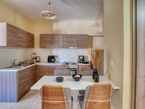 Uma cozinha moderna com armários de madeira, bancada branca, mesa de jantar com duas cadeiras e luminária pendente.