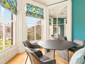 A dining area with a table and chairs, large windows with curtains, and a view of the outside.