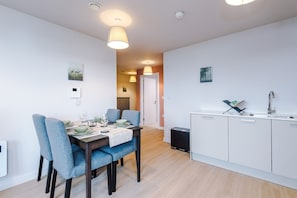 A modern kitchen with white cabinets, a sink, and a dining area with blue chairs and a table set for four. - 2BDR Old Trafford Free Parking Rooftop Terrace (Stretford)