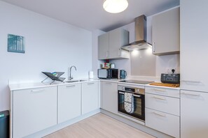 Eine moderne Küche mit weißen Schränken, einer Edelstahl-Spüle, einer Mikrowelle, einem Backofen und einer Kaffeemaschine.