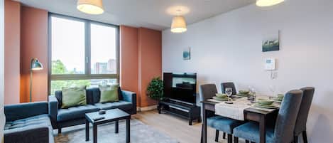 A modern living room with a sofa, coffee table, TV, and dining area with chairs and table set.