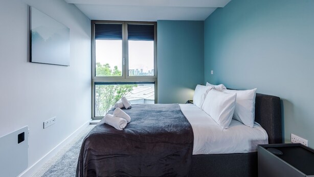 Een slaapkamer met een bed, een raam en een wandlamp.