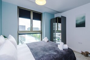 A hotel room with a large bed, a view of the city, a window with blinds, and a painting on the wall. - 2BDR Old Trafford Free Parking Rooftop Terrace (Stretford)