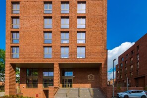 A multi-story brick building with a central entrance, large windows, and a visible logo on the facade. - 2BDR Old Trafford Free Parking Rooftop Terrace (Stretford)
