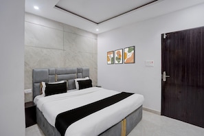 Une chambre moderne avec un grand lit, une porte en bois foncé et trois œuvres d’art encadrées accrochées au mur.