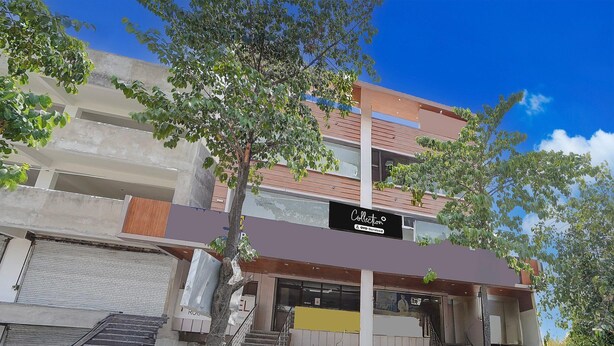 Un edificio de varias plantas con un diseño arquitectónico moderno, que cuenta con una entrada destacada con una escalera, un letrero visible y un cielo despejado.