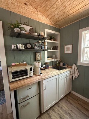 Una cocina con horno integrado, una cafetera y diversos utensilios de cocina en estantes.