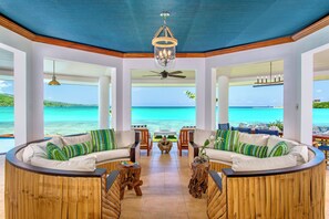 A spacious room with a curved sofa set, wooden accents, and a view of the ocean. - Oceanfront Paradise staffed 4 bedroom Home Views Pool Beach Access Gym Tennis (Montego Bay)