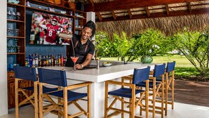Eine Bar mit Theke, einem Barkeeper, einem Fernsehbildschirm, der ein Fußballspiel zeigt, und Außenplätzen.