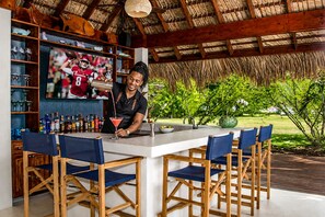 Eine Bar mit Theke, einem Barkeeper, einem Fernsehbildschirm, der ein Fußballspiel zeigt, und Außenplätzen.
