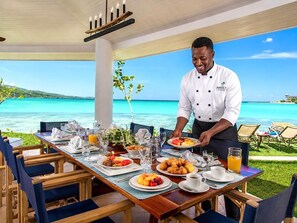 Ein Koch serviert Frühstück an einem Tisch mit Blick aufs Meer.