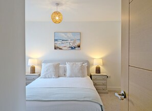 Ein Schlafzimmer mit einem Bett, zwei Nachttischen, einer Wandlampe, einem Gemälde und einer Tür.