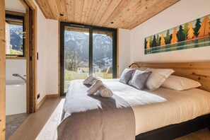 Ein Schlafzimmer mit Holzboden, einem Bett mit Kissen, einem Fenster mit Bergblick und einem Bild an der Wand.
