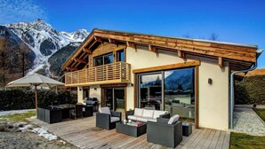 A modern chalet with a wooden deck, outdoor seating, and a mountain backdrop. - Clarines · Where the Fields Meet Mont Blanc (Chamonix)