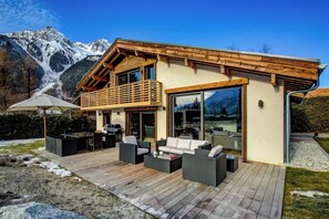 Eine moderne Chalet mit einer Holzterrasse, Sitzgelegenheit im Freien und Bergblick.