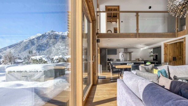 A modern interior with a large glass door leading to a snowy mountain view, a cozy seating area, and a kitchen. - Clarines · Where the Fields Meet Mont Blanc (Chamonix)