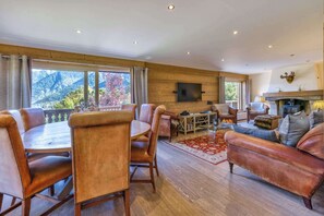 A spacious living area with a wooden floor, leather furniture, a fireplace, and a large window with a mountain view.