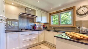 Een moderne keuken met witte kasten, een roestvrijstalen afzuigkap, een raam met uitzicht op groen en een klok aan de muur.