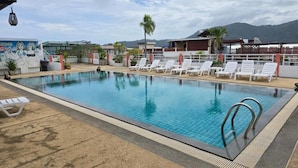 A swimming pool with lounge chairs, a covered area, and a view of mountains. - Blue Sapphire Hotel (Patong)