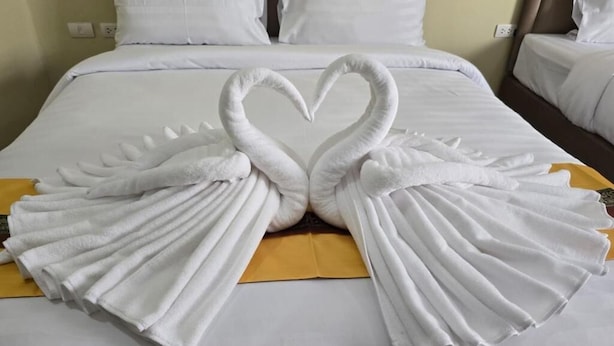 A bed with white linens and a heart-shaped towel arrangement. - Blue Sapphire Hotel (Patong)