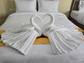 A bed with white linens and a heart-shaped towel arrangement.