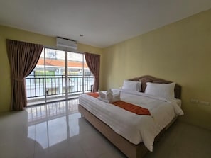 A bedroom with a large bed, a balcony with curtains, and an air conditioning unit.