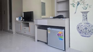 A room with a kitchenette, a television, a refrigerator, a mirror, and a wall with a floral painting. - Blue Sapphire Hotel (Patong)