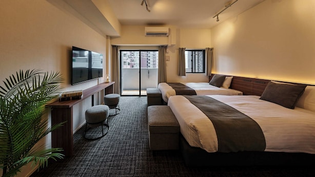 Habitación de hotel con dos camas, televisor, escritorio y planta.