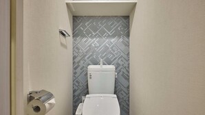 Un baño pequeño con inodoro, accionador de descarga en la pared y un revestimiento de pared estampado.