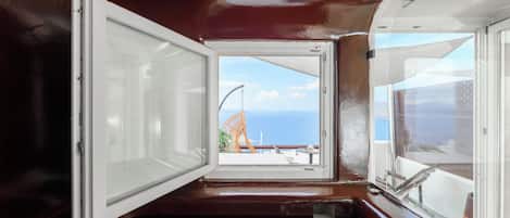 Una habitación con un amplio ventanal, vista al mar y un balcón con una silla.