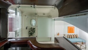 A modern interior with a glass partition, a seating area with cushions, a wall-mounted mirror, and a potted plant. - Sophia Oia Suites (Oia)