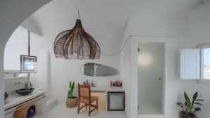 A modern bathroom with a white vanity, a mirror, a sink, a towel rack, and a shower area. - Sophia Oia Suites (Oia)