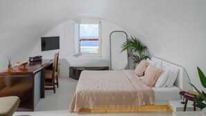 A bedroom with a bed, a desk, a chair, a TV, and a window with a view. - Sophia Oia Suites (Oia)