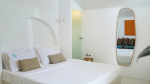 A bedroom with a bed, a small bedside table, a mirror, and a wall with a light switch. - Sophia Oia Suites (Oia)