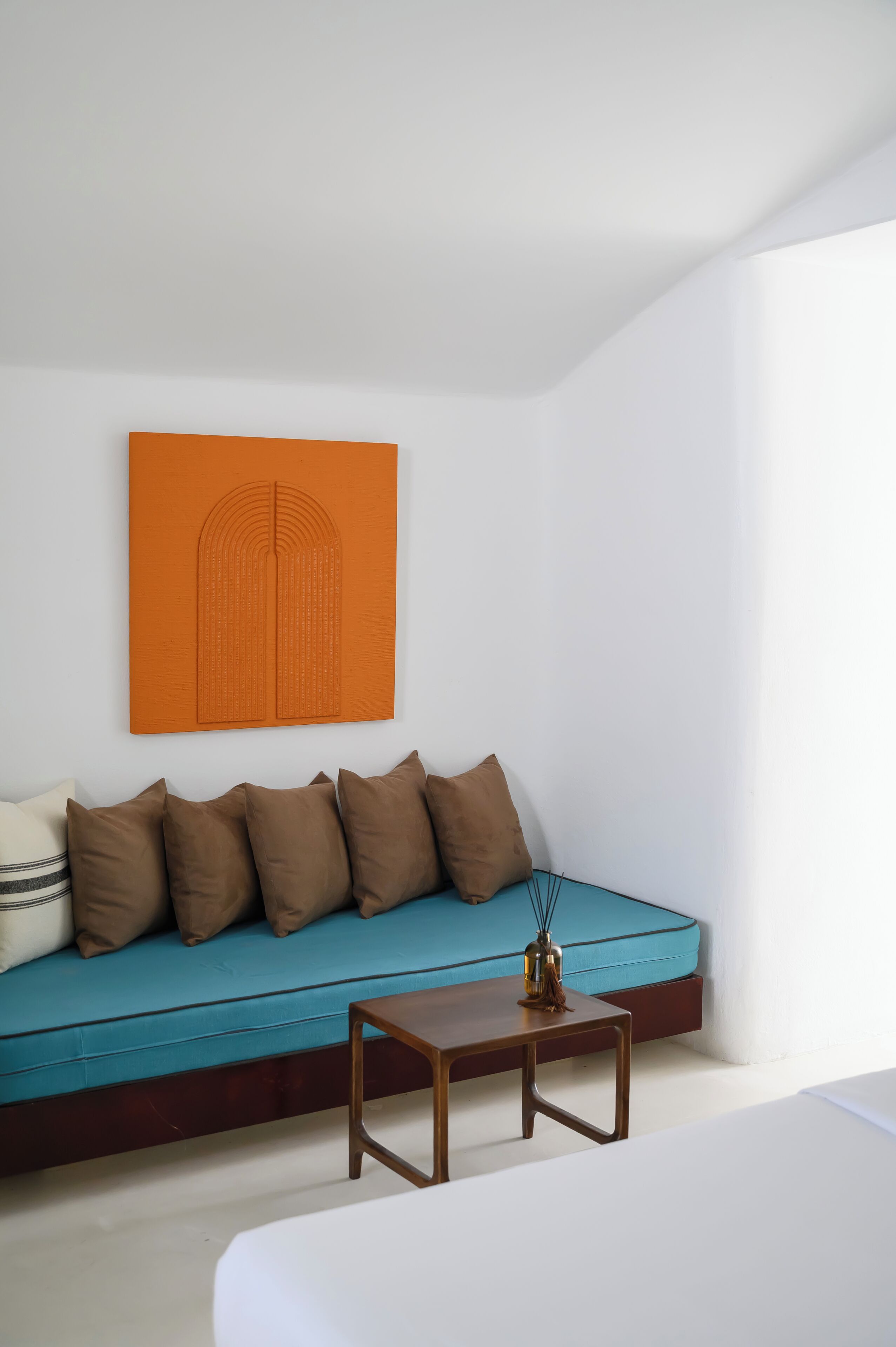 Ein modernes Zimmer mit einem petrolfarbenen Sofa, einem Holztisch und einem orangefarbenen Kunstwerk an der Wand.
