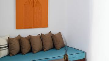 Ein modernes Zimmer mit einem petrolfarbenen Sofa, einem Holztisch und einem orangefarbenen Kunstwerk an der Wand.