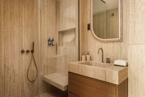Ein modernes Badezimmer mit einer gläsernen Duschkabine, einem Waschtisch mit Marmorplatte und einem Spiegel mit Holzrahmen.
