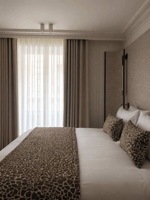 A hotel room with a large bed, a headboard, a window with sheer curtains, and a wall-mounted lamp. - Madame Luxury 3BR 6P with AC (Paris)