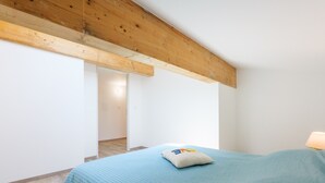 A bedroom with a bed, a pillow, a wooden ceiling beam, and a door leading to another room. - Holiday Home 'Le Gecko' with Private Terrace and Wi-Fi (Saint-Germain)