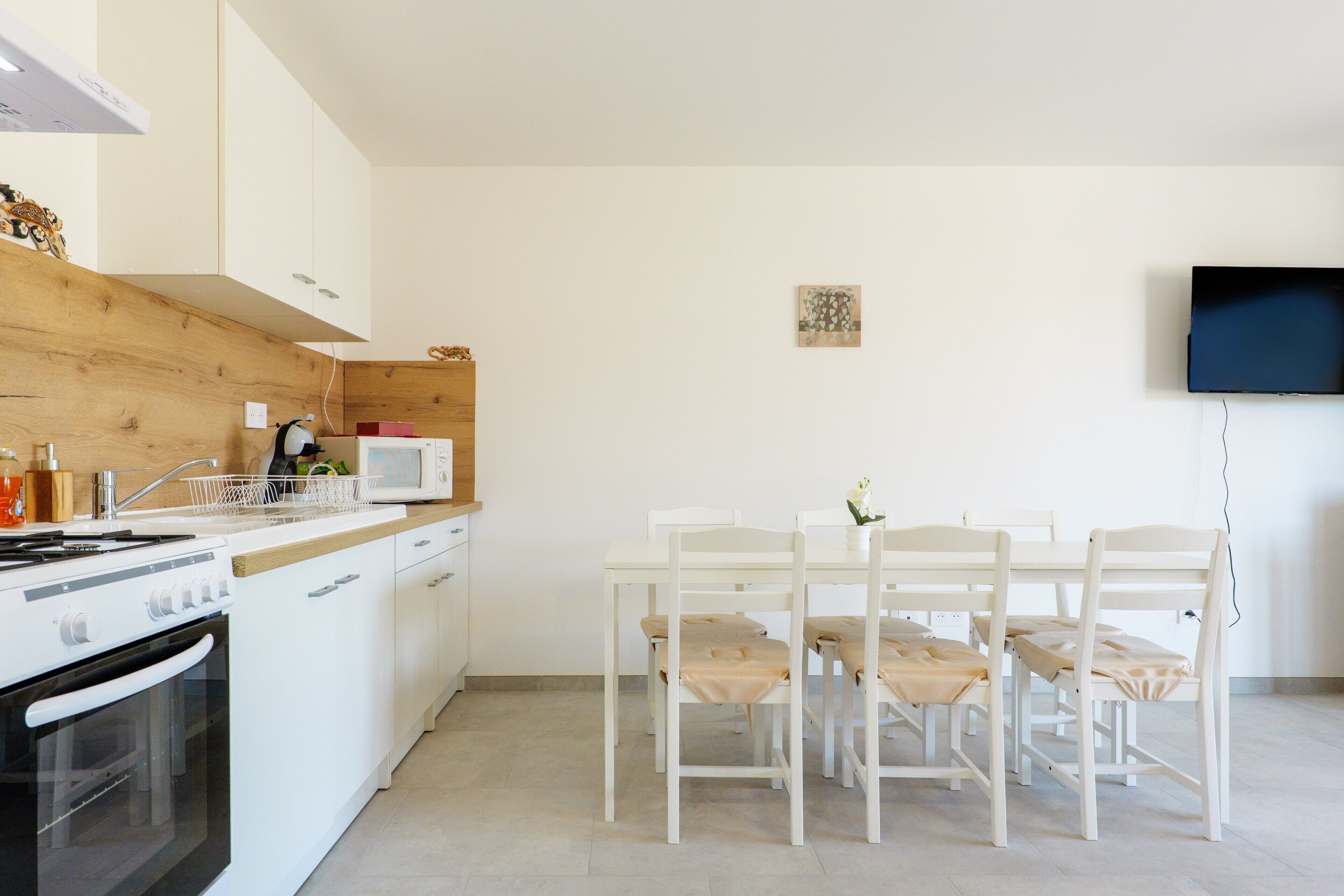 Une cuisine moderne avec des meubles blancs, un plan de travail en bois et un coin repas avec des chaises blanches.
