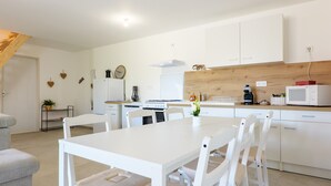 A modern kitchen with white cabinetry, a dining table, and chairs. - Holiday Home 'Le Gecko' with Private Terrace and Wi-Fi (Saint-Germain)
