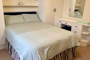 Een slaapkamer met een bed, een dressoir, een spiegel en een plank.