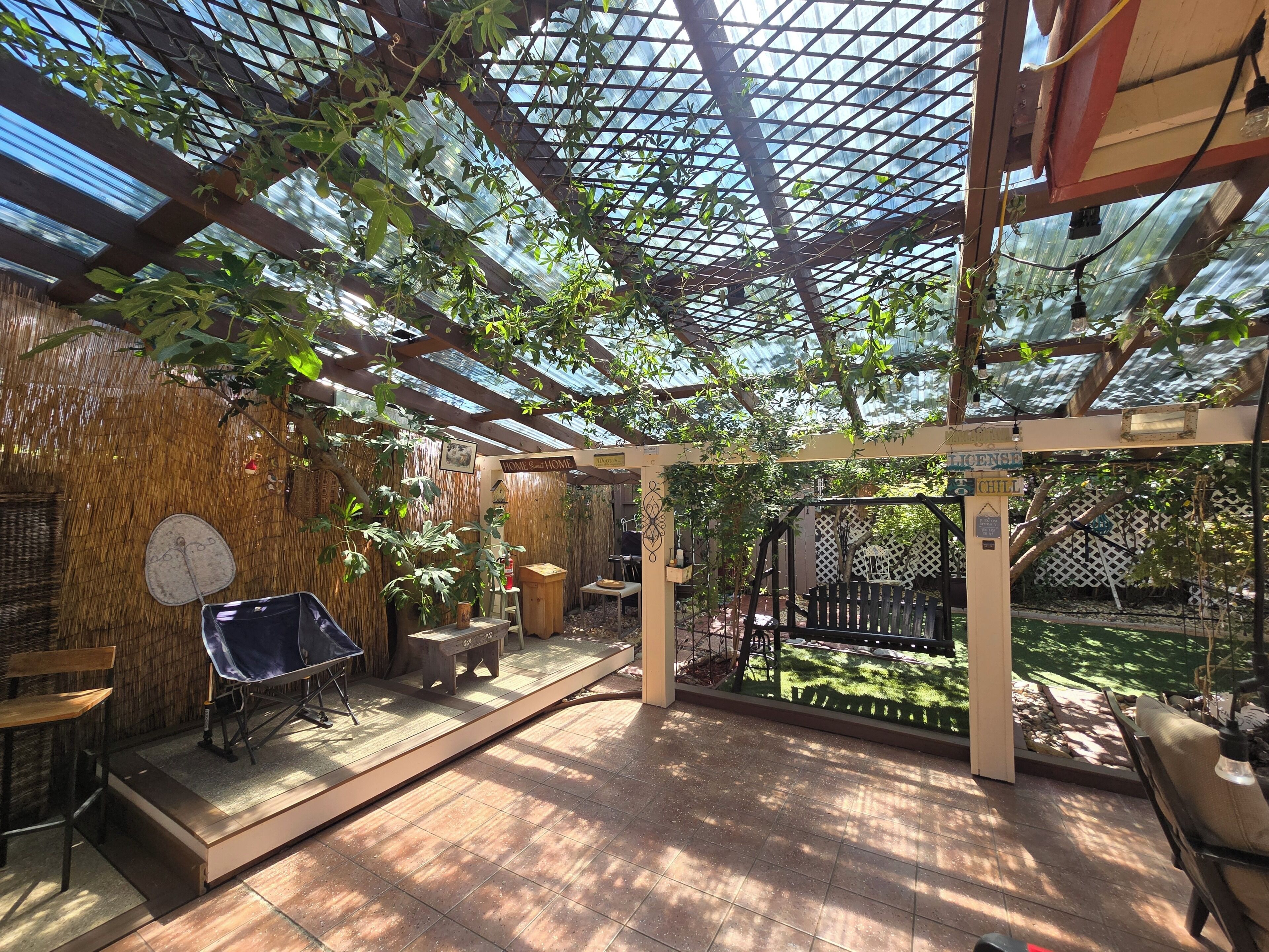 Un espace extérieur abrité, doté d’un plancher en bois, d’une table, de chaises et d’une pergola couverte de plantes grimpantes.