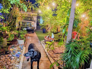 Ein gepflasterter Weg in einem Garten mit einem Hund, Blumentöpfen und einem Fahrzeug im Hintergrund.