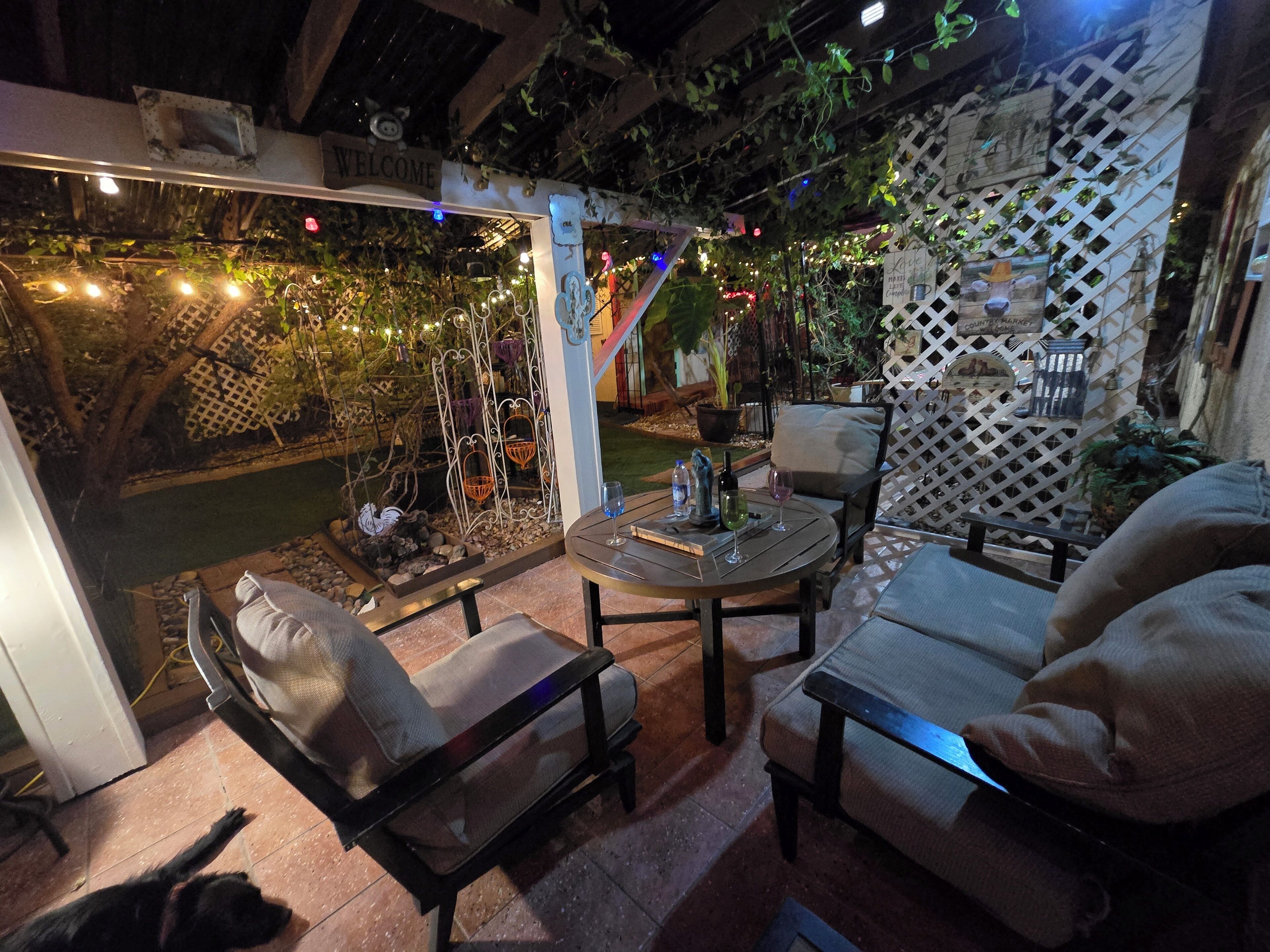 An outdoor patio with a round table, two chairs, a dog, and a decorative fence.