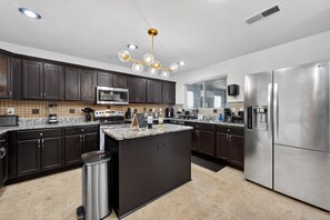 A modern kitchen with dark cabinets, granite countertops, stainless steel appliances, and a central island. - Southern Comfort Escapes 5br For 14 Near Nasa 5 Bedroom Home (Madison)