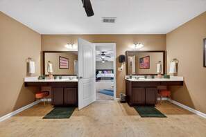 A hotel room with two bathrooms, a ceiling fan, a bed with a blue rug, and a small trash can. - Southern Comfort Escapes 5br For 14 Near Nasa 5 Bedroom Home (Madison)