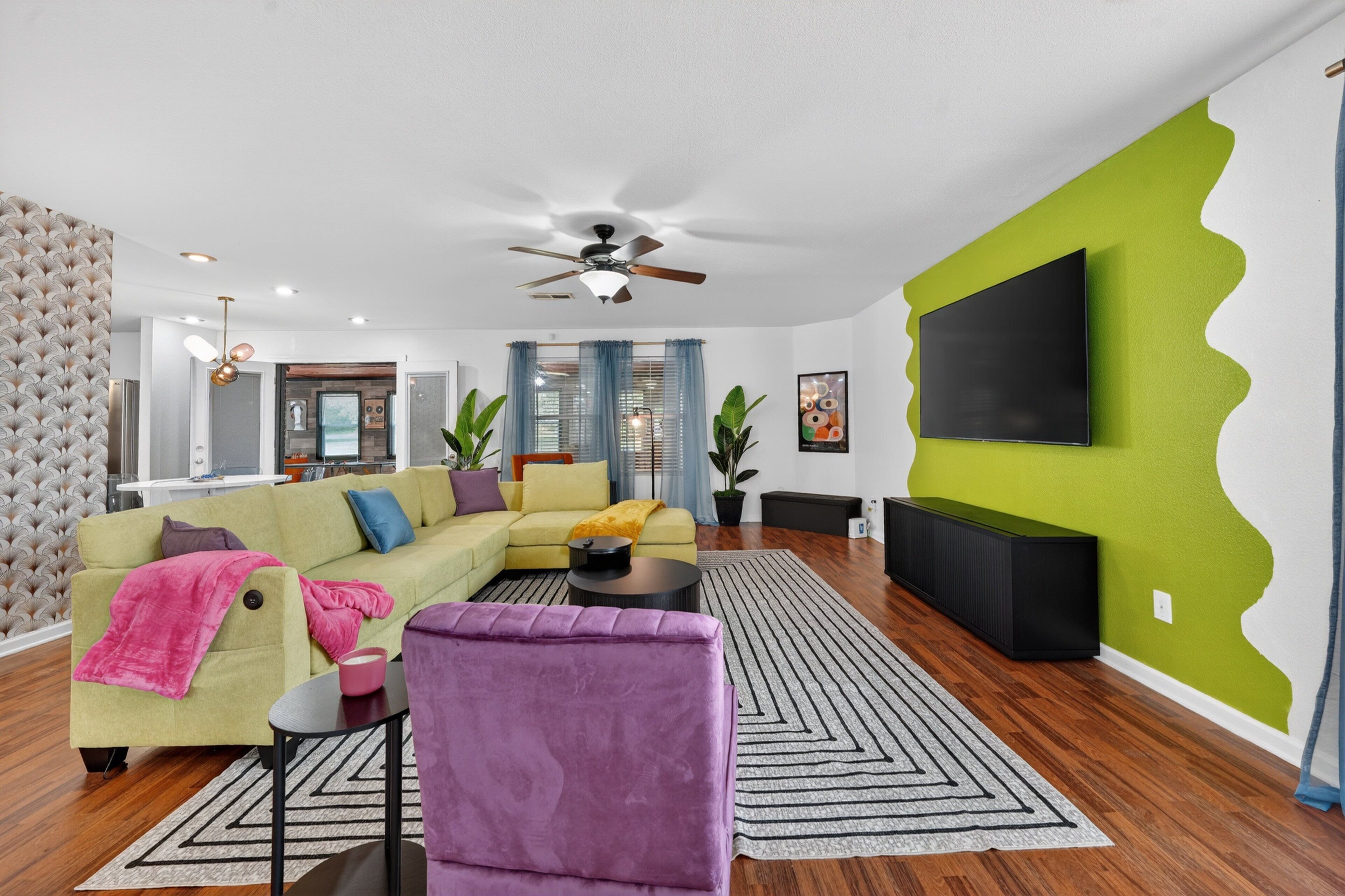 A modern living room with a sectional sofa, a purple armchair, a flat-screen TV, and a ceiling fan.