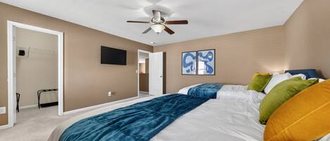 A bedroom with a bed, ceiling fan, artwork, and a door leading to another room.